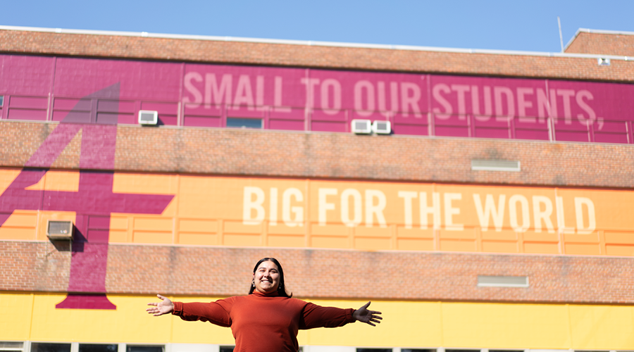 Augsburg Student standing with her arms wide open in front of the mural in the quad